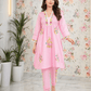 Woman wearing a pink embroidered outfit in a room with floral wallpaper.